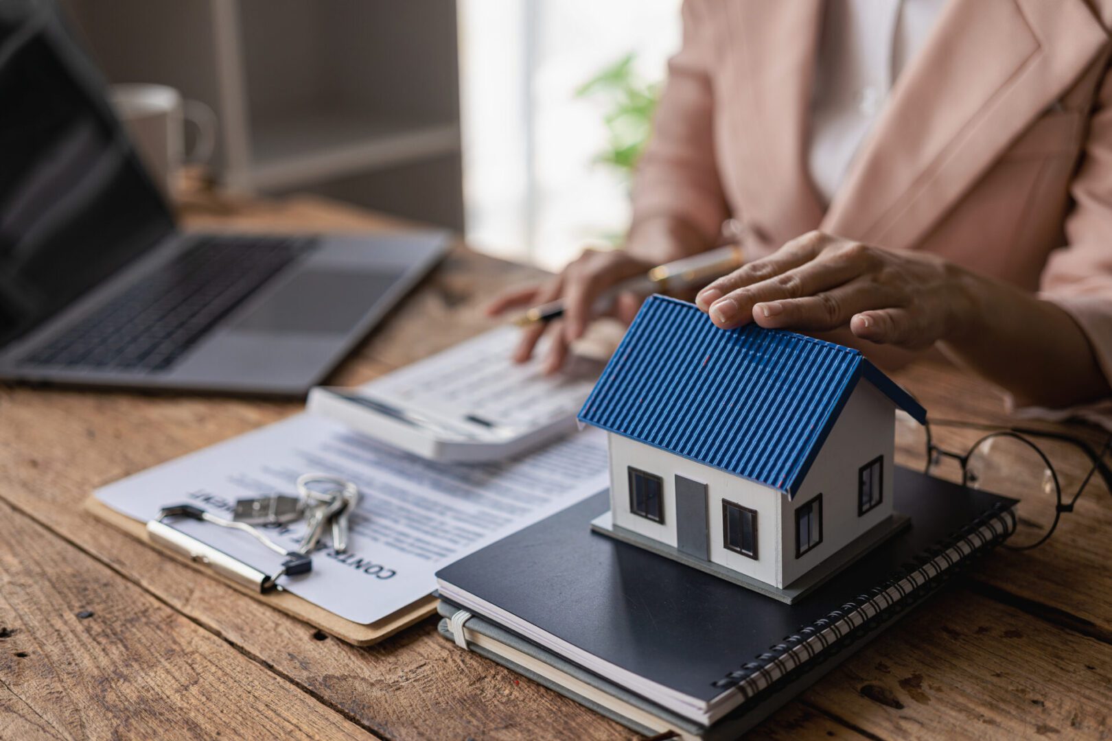 Person calculating with house model on desk.