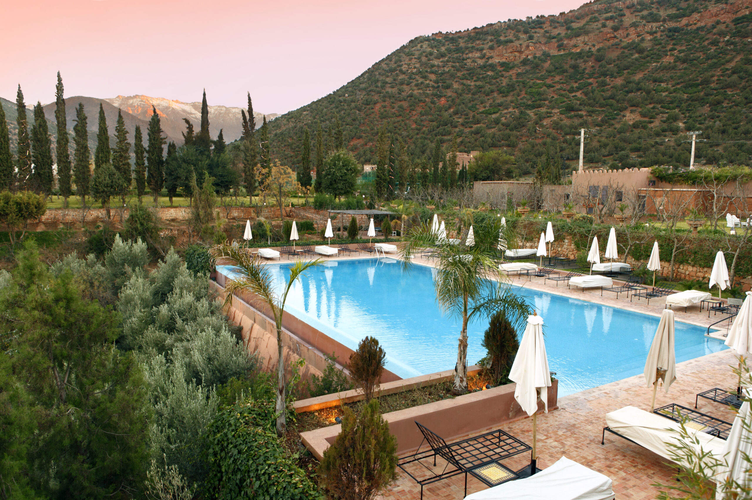 A luxury resort pool in the Atlas Mountains of Morocco at sunset.