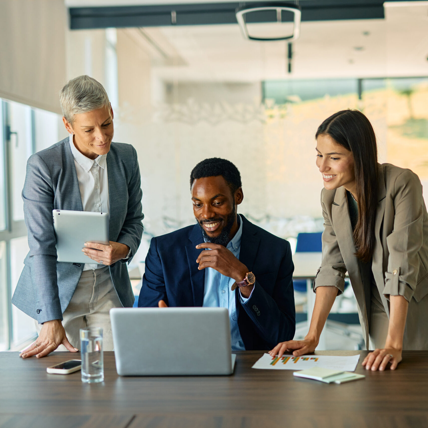 Three business professionals collaborating in a modern office, utilizing a laptop and digital tablet for data analysis and strategic development, fostering effective communication and teamwork