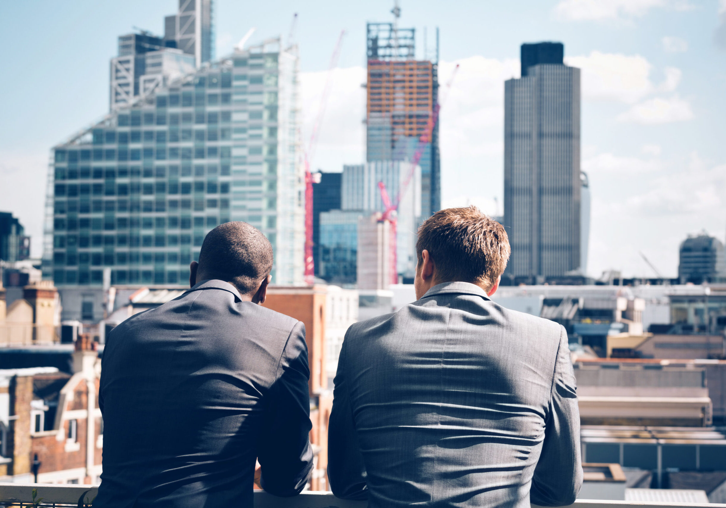 Back view of two businessmen - caucasian and afro american - standing outdoor and looking at city scape.